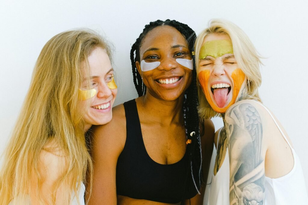 Monthly Horoscope Hub Skin Care. Three women are having fun with colorful skincare masks, embodying friendship and joy.