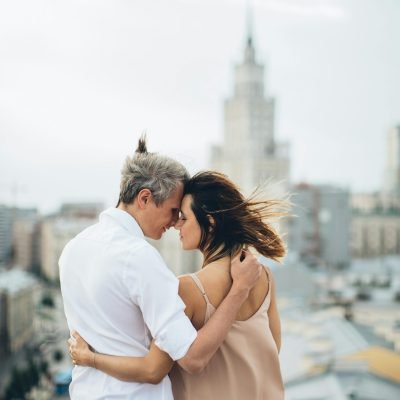 A loving couple shares an intimate moment on a city rooftop with a blurred cityscape in the background.